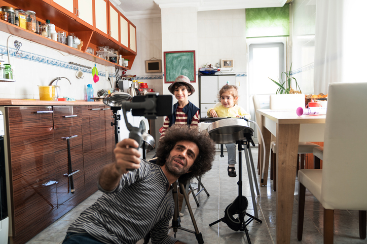 parent holding selfie stick in kitchen with two children