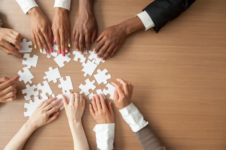 group of Black and white people joining puzzle pieces at desk