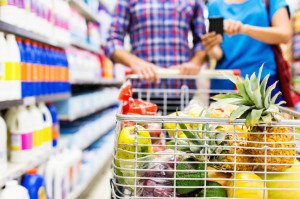 Fruit in cart with couple using smartphone at supermarket
