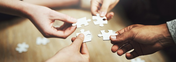 Cropped shot of a group of unrecognizable people fitting puzzle pieces together on the floor