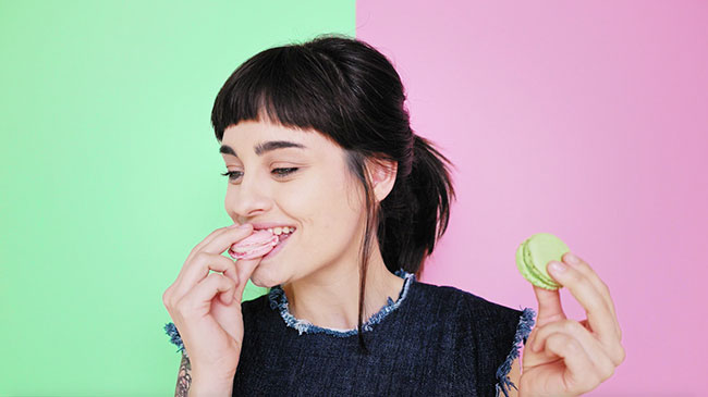 Woman eating macaroons in front of pastel background