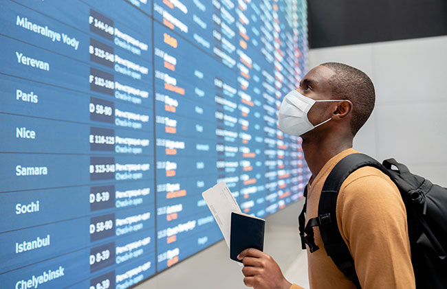 Person wearing mask looking at flight board in airport